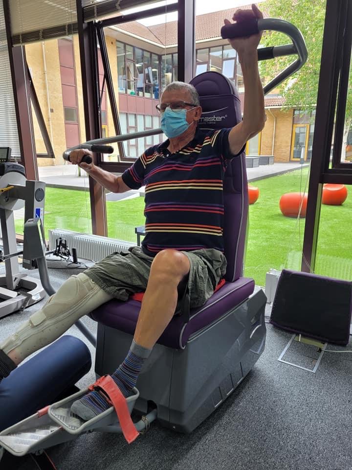 A male service user wearing a mask uses the Shapemaster equipment, which is now available for independent exercise between therapy sessions.