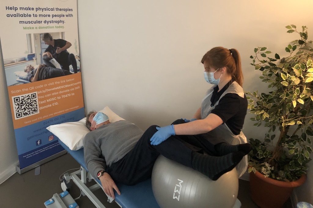 A man lying on a bed having physiotherapy. He and the physiotherapists are wearing face masks.