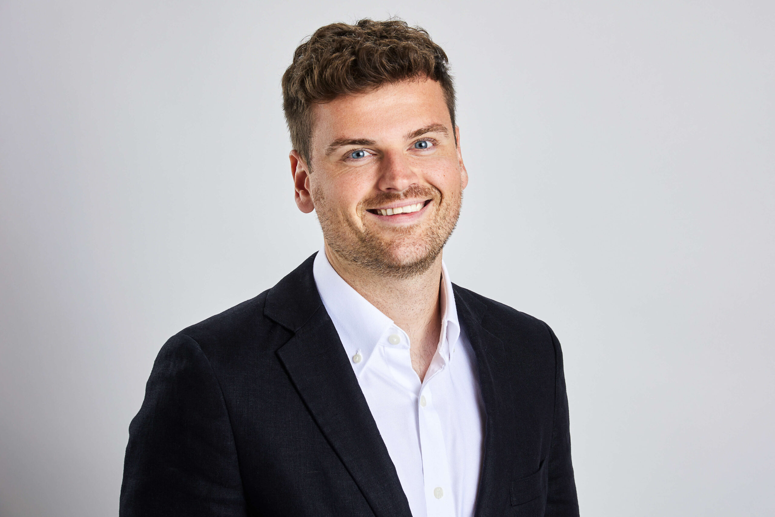 James Mckay is smiling at the camera. He is dressed in smart casual clothers and has short brown hair