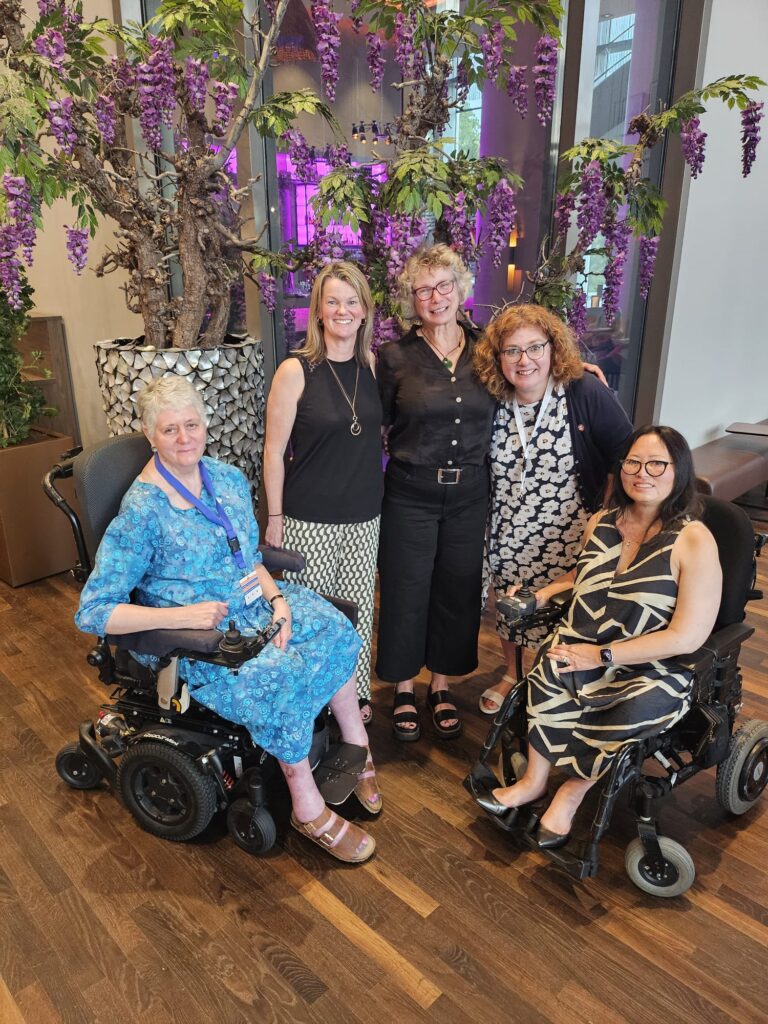 A group of people at FSHD Connect. Two are in power chairs. All are smiling at the camera and dressed as if going for dinner.