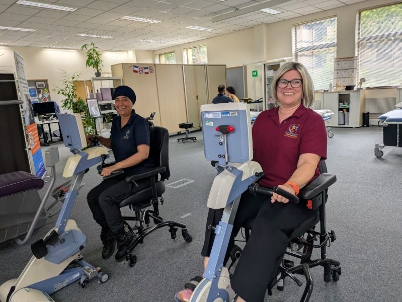 Two people using accessible bikes, pedalling with their arms. They are wearing MDSC branded t-shirts