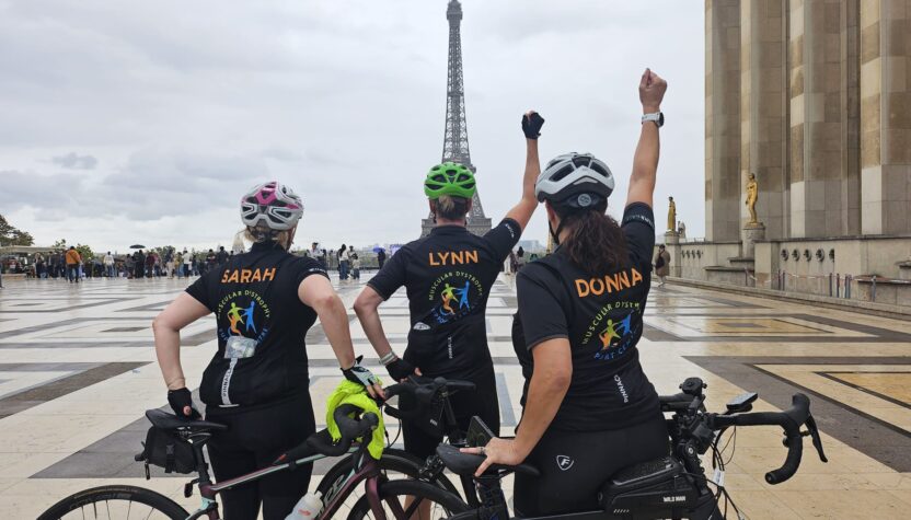 Sarah, Lynn, and Donna with their bikes in front of the Eiffel Tower. They have their back to the camera and are facing the tower with their hands raised in celebration,