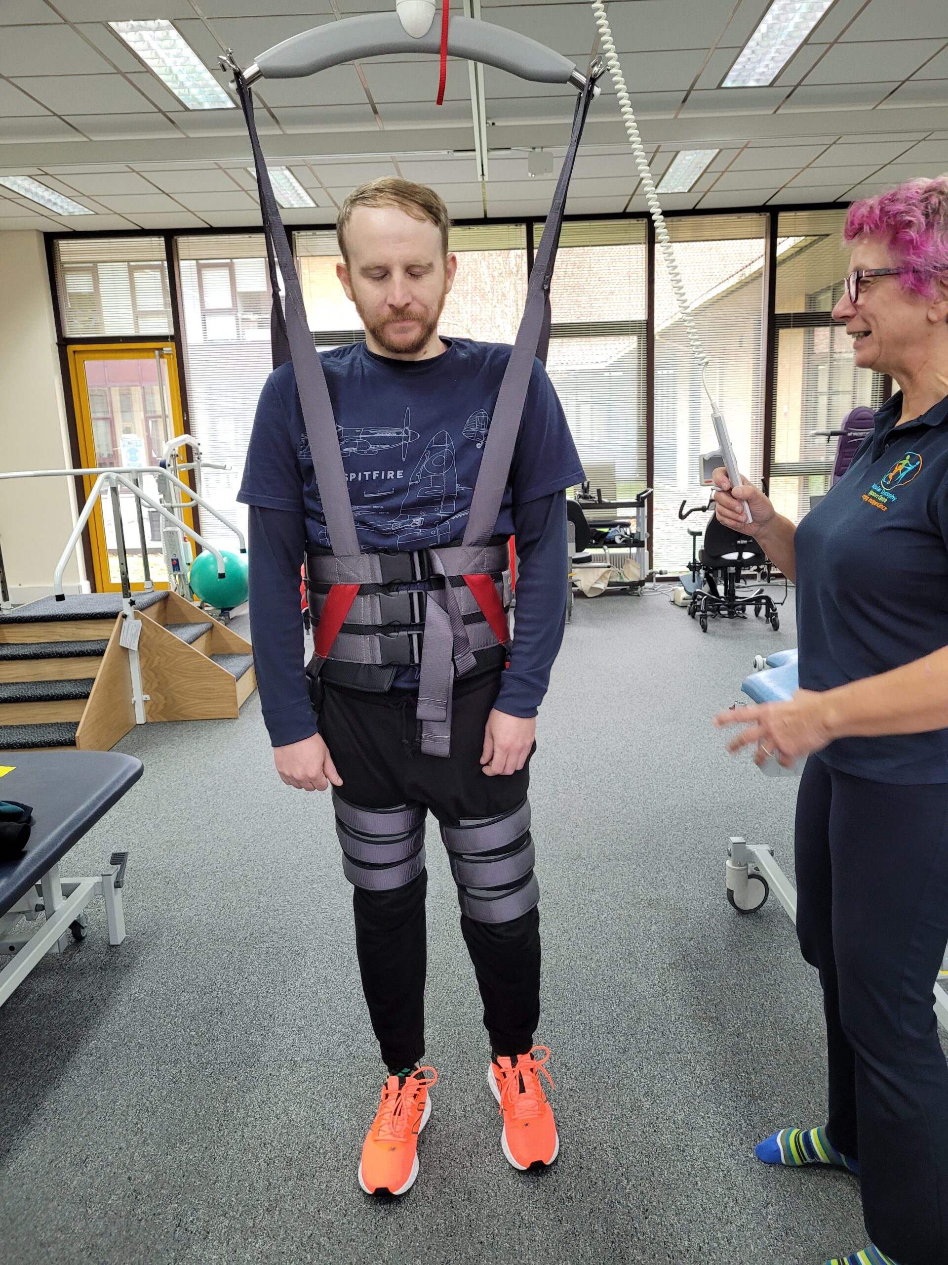 A physiotherapist supports a service user to walk using a ceiling tracked hoist