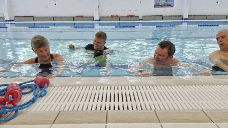 Three people in a swimming pool supported by a physiotherapist. The physiotherapist is supporting a woman while the others exercise next to her