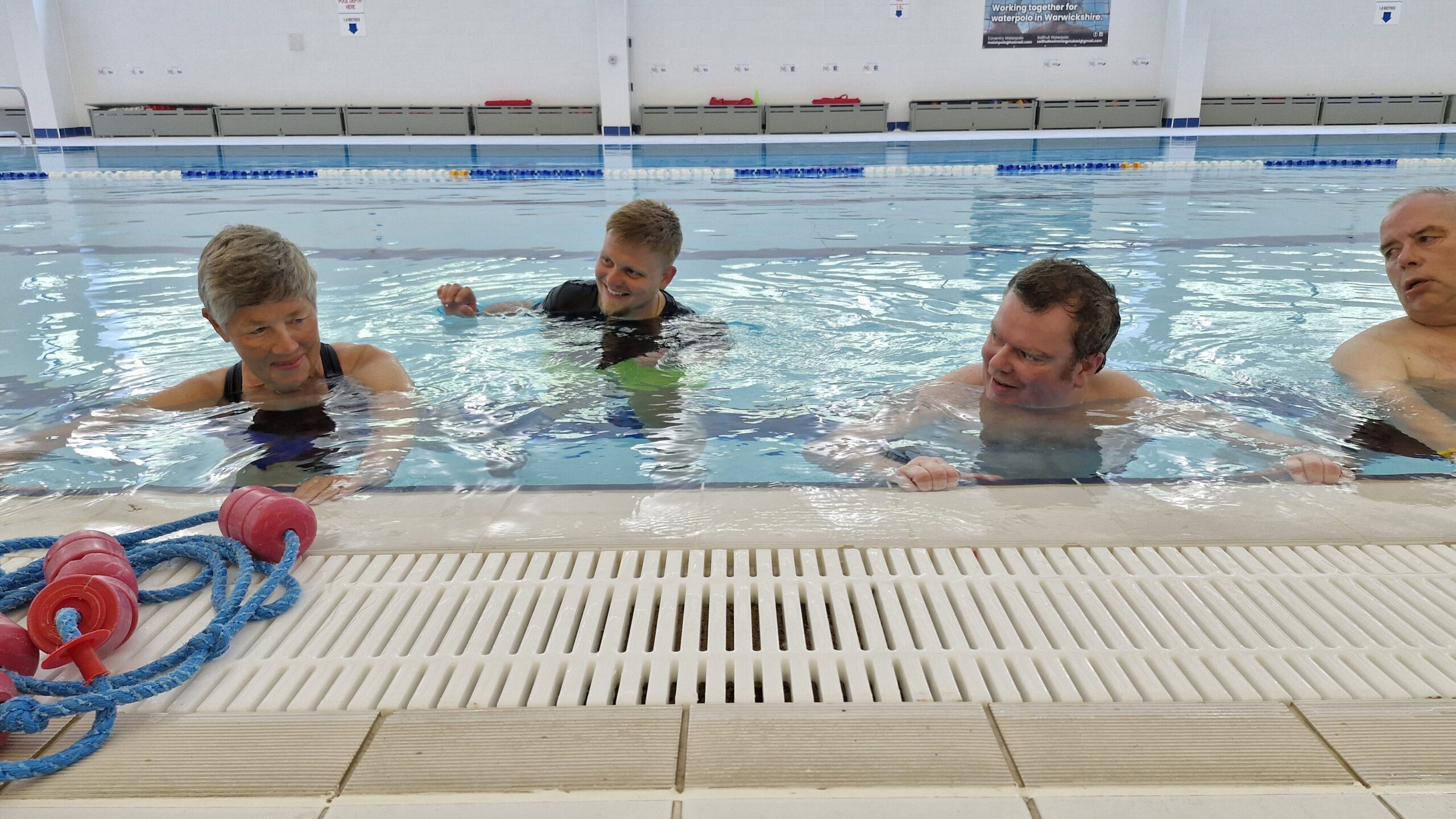 Three people in a swimming pool supported by a physiotherapist. The physiotherapist is supporting a woman while the others exercise next to her
