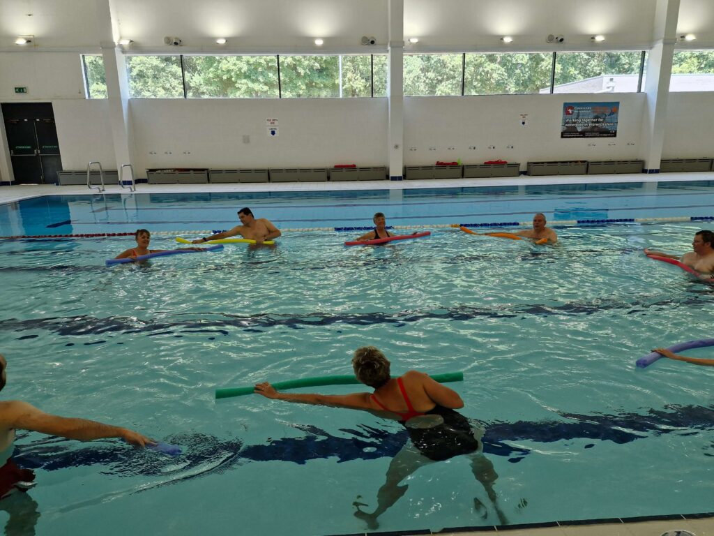 A group of people exercising in a swimming pool using pool noodles