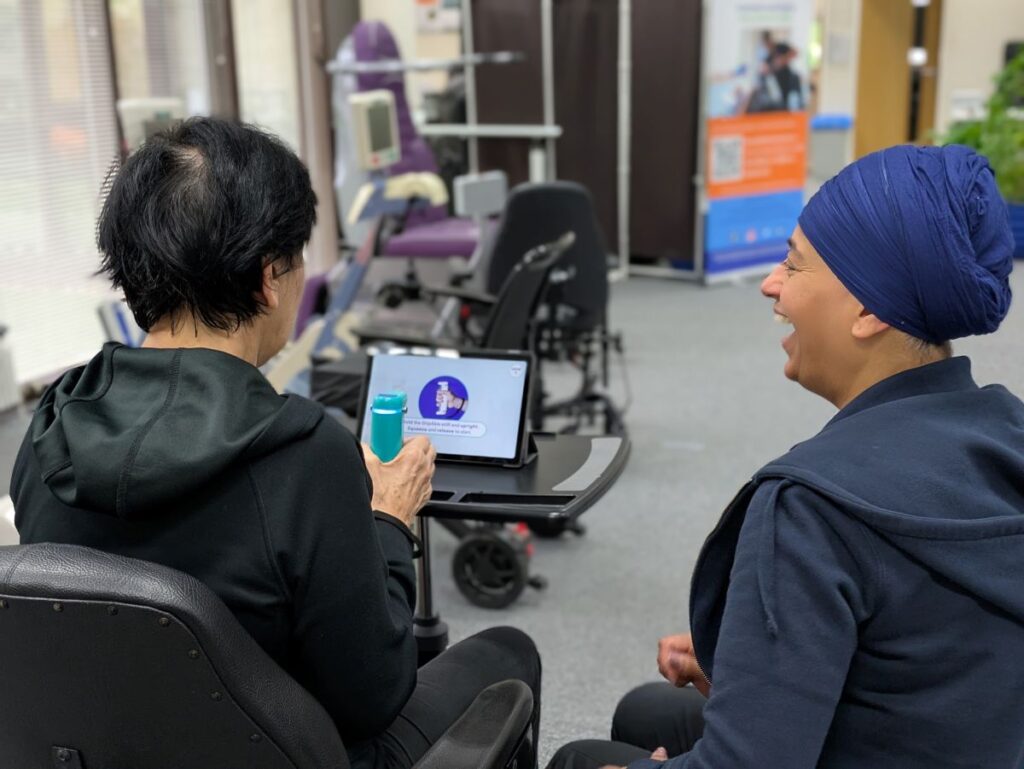 A service user having hand therapy with our therapy assistant. They are using the gripable device to operate a tablet pc. The therapy assistant is laughing.