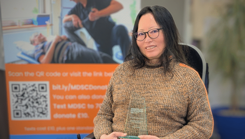 A woman seated in front on an MDSC promotional banner holding an award.